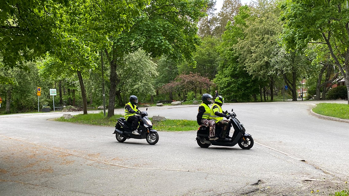 Tre personer kör mopedbilar i trafik under övningskörning.