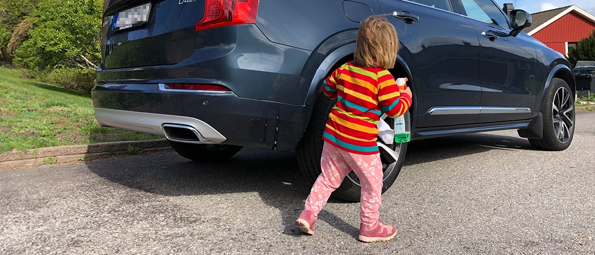 Litet barn i färgglada kläder står nära en parkerad bil