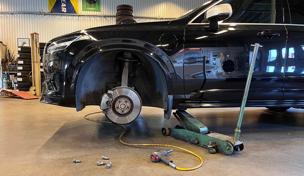 Bil løftet i verksted med fjernet hjul og synlige bremser