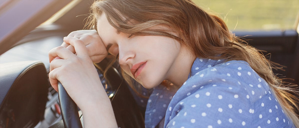 Trött kvinna i bil lutar sitt huvud mot ratten