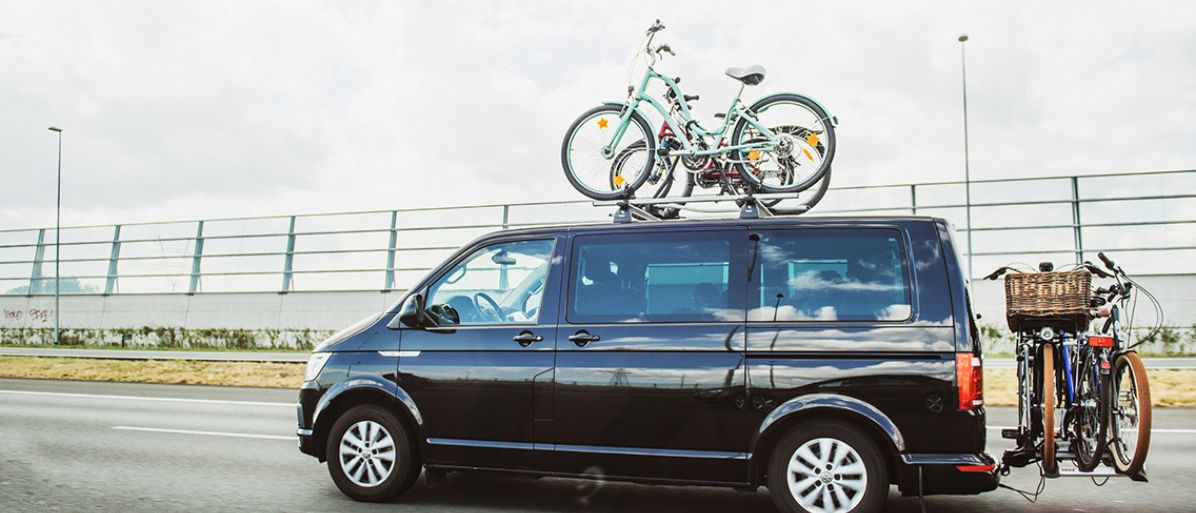 Svart bil med två cyklar monterade på taket kör på en väg