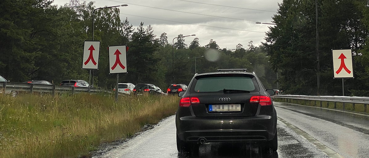 Bilar i kö på en väg med vägskyltar som visar sammanflöde av trafik