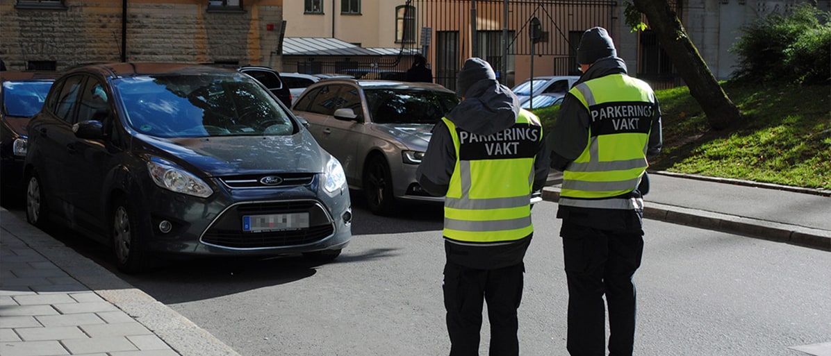 Parkeringsvakter i reflexvästar skriver ut en parkeringsbot vid en bil
